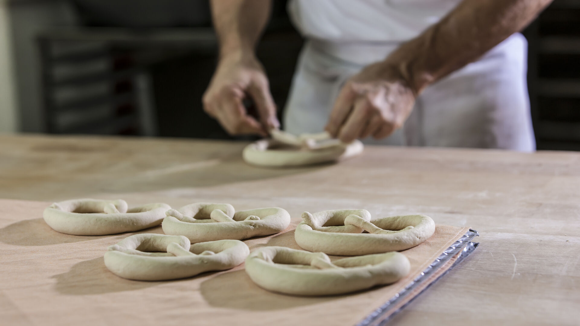 Hände formen rohe Brezn aus Teig auf einer bemehlten Arbeitsfläche